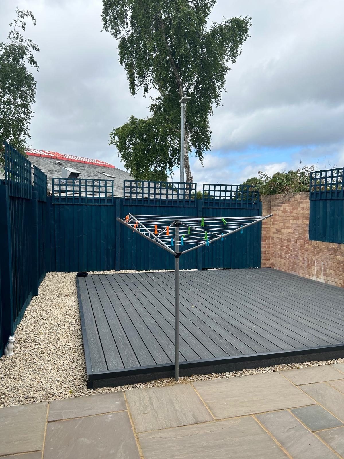 Large dark composite decking area enclosed by painted fencing and gravel