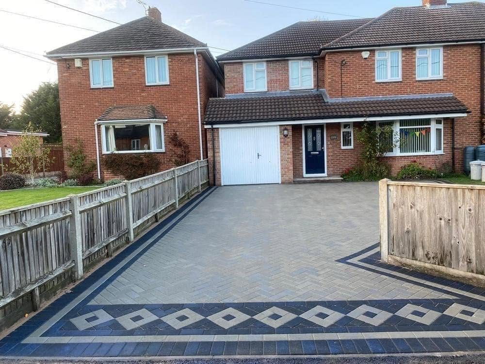 Large grey patterned block paving driveway between two brick homes