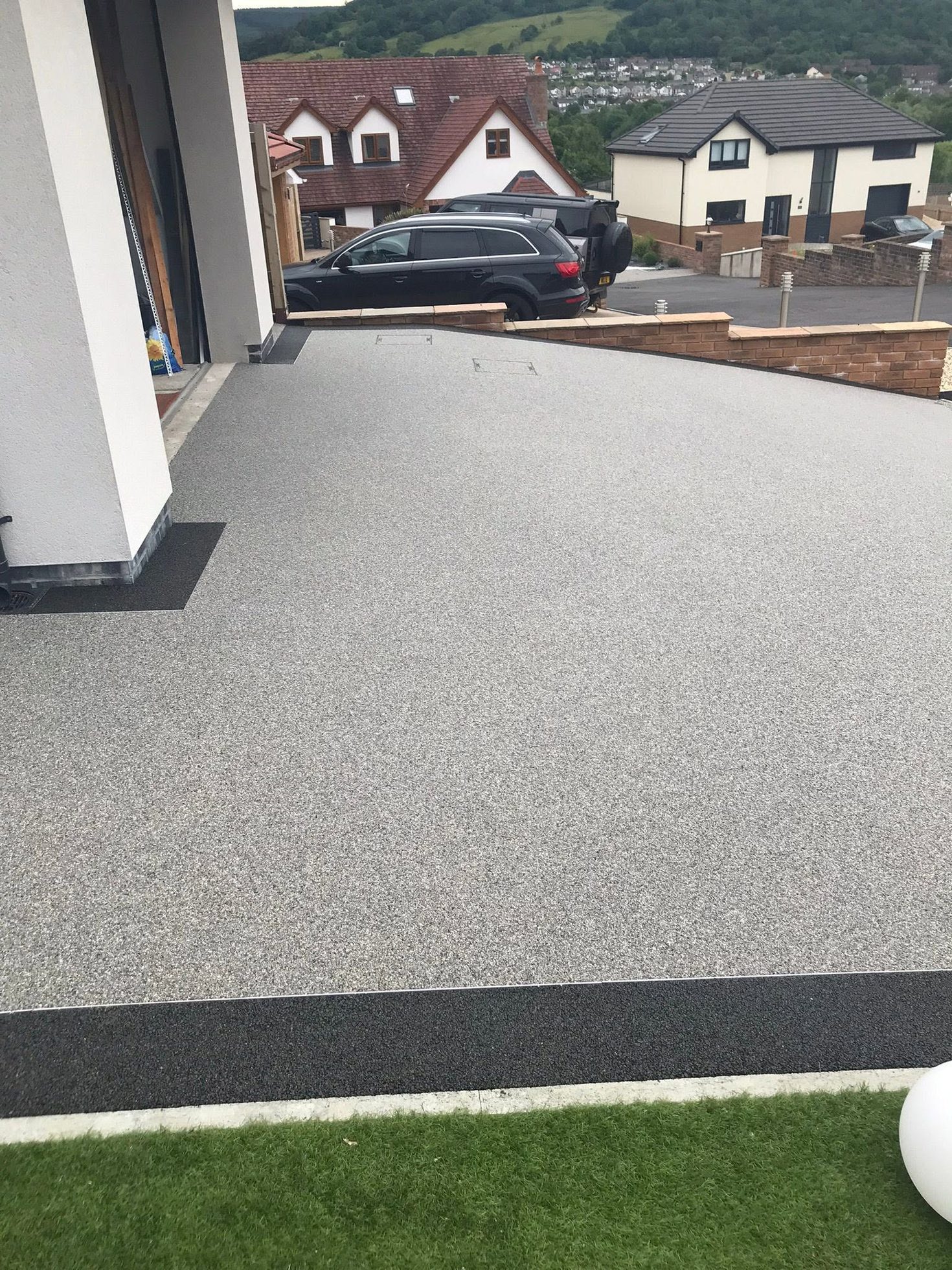 Large light grey resin bound driveway on a sloped residential property