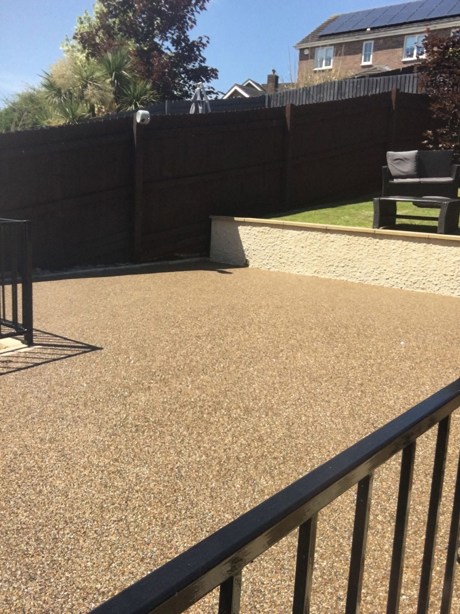Tan resin bound garden patio surface laid beside dark fencing and a lawn