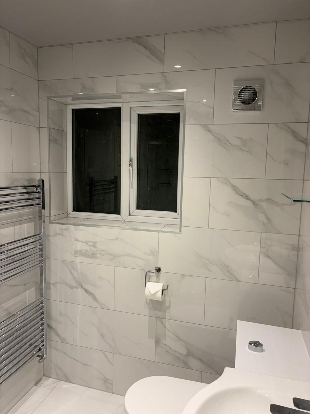 Marble effect tiled bathroom with chrome heated towel rail, toilet and sink