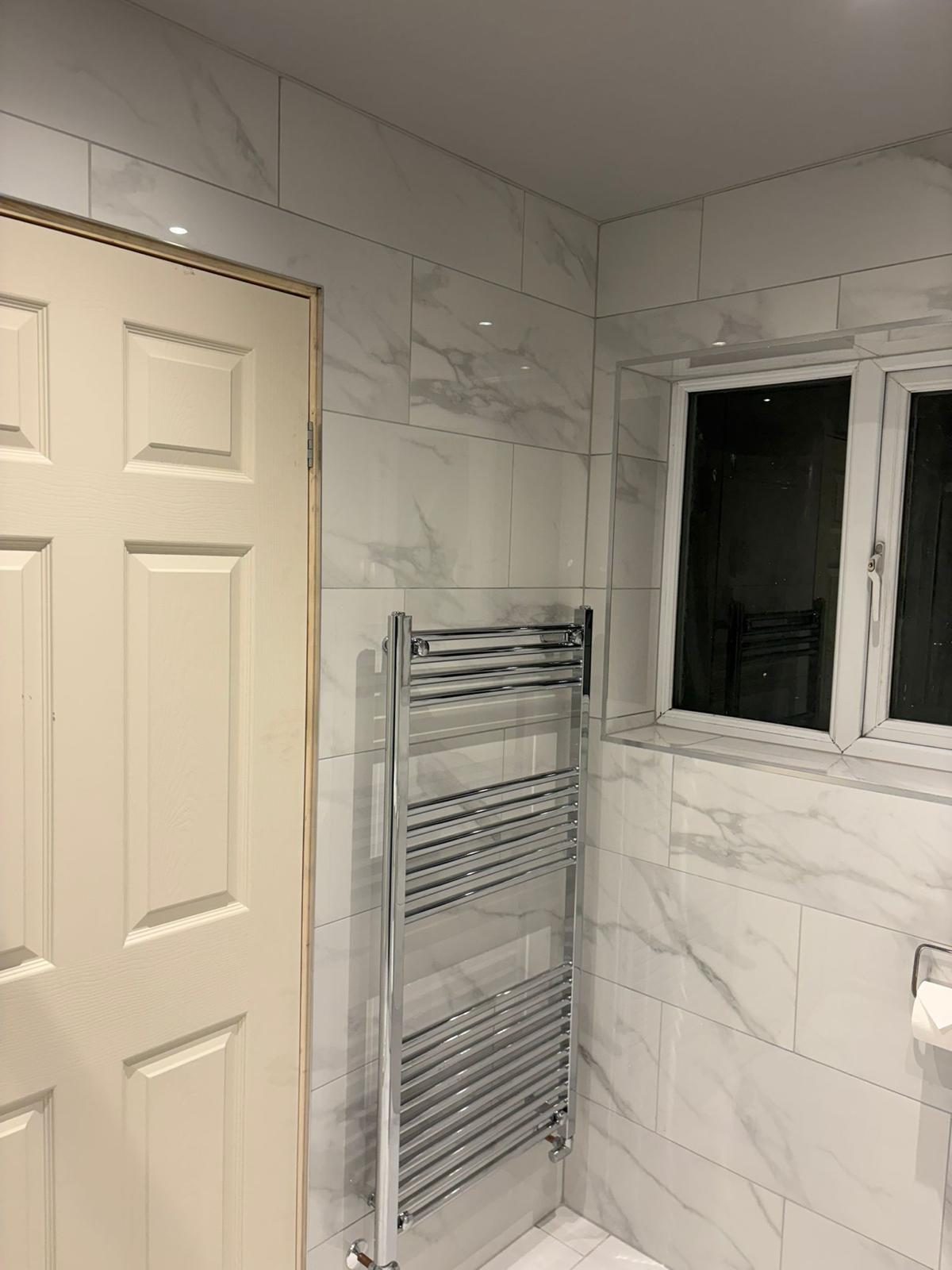 Newly tiled bathroom with chrome towel radiator and white internal door