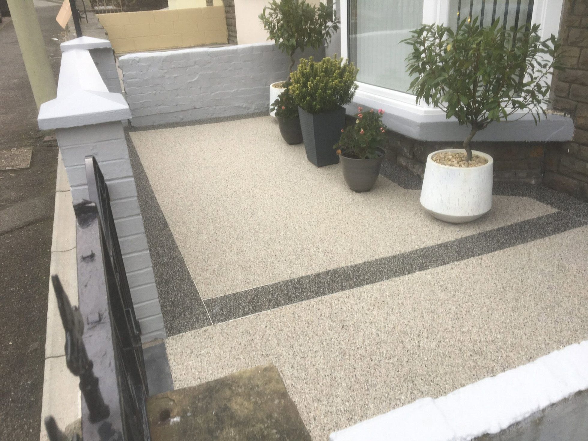 Light resin bound patio with dark edging and potted plants beside a house