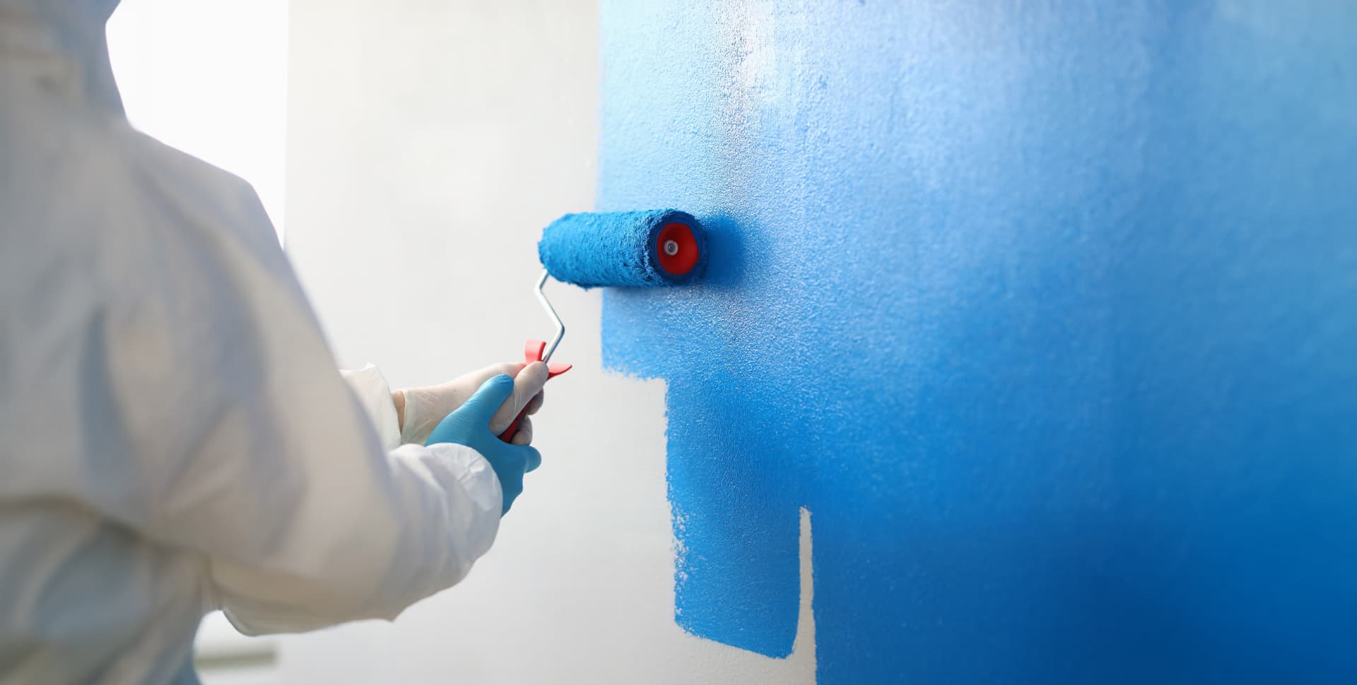 Decorator rolling fresh blue emulsion onto an interior wall