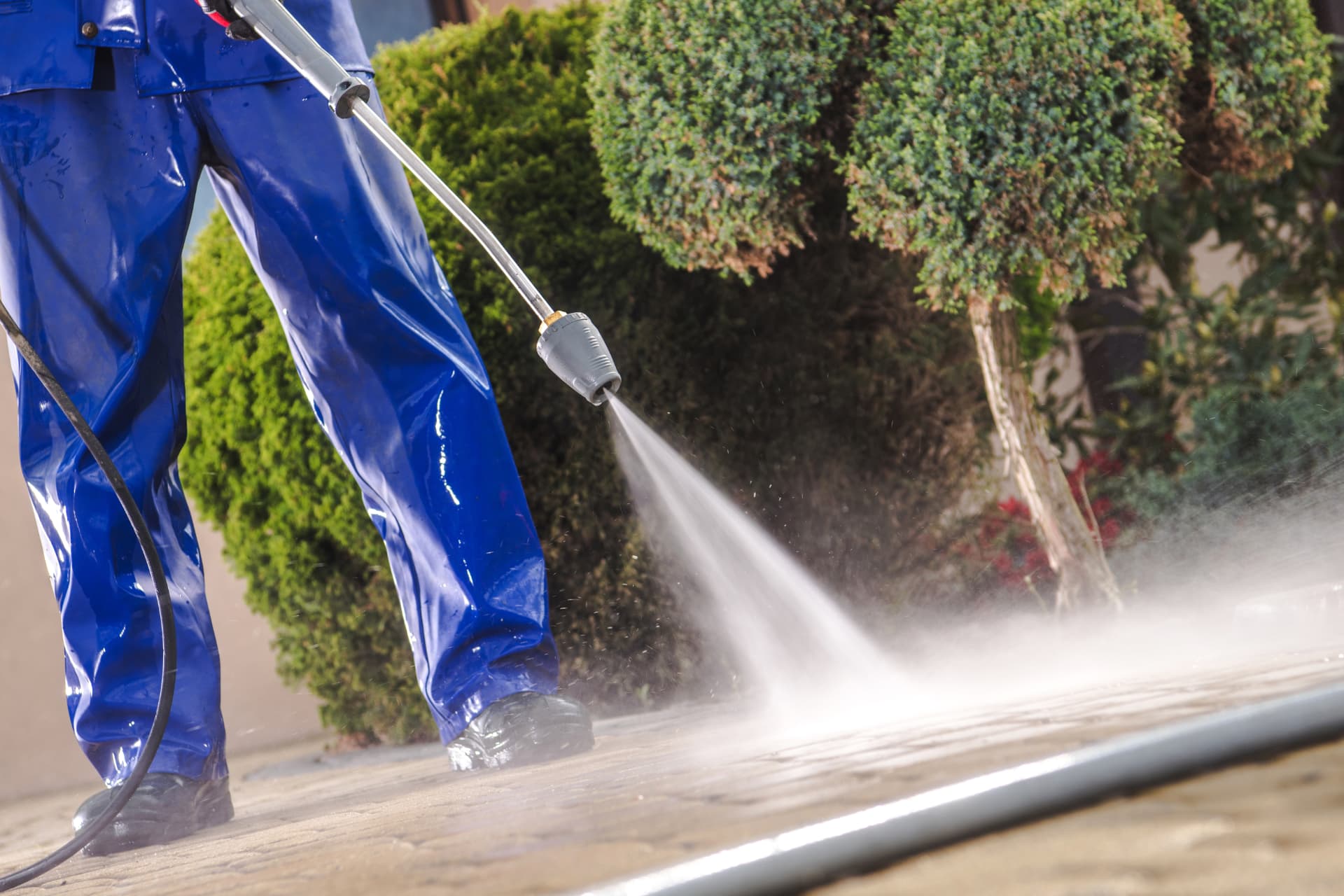 Pressure washer cleaning a paved driveway surface outside a house
