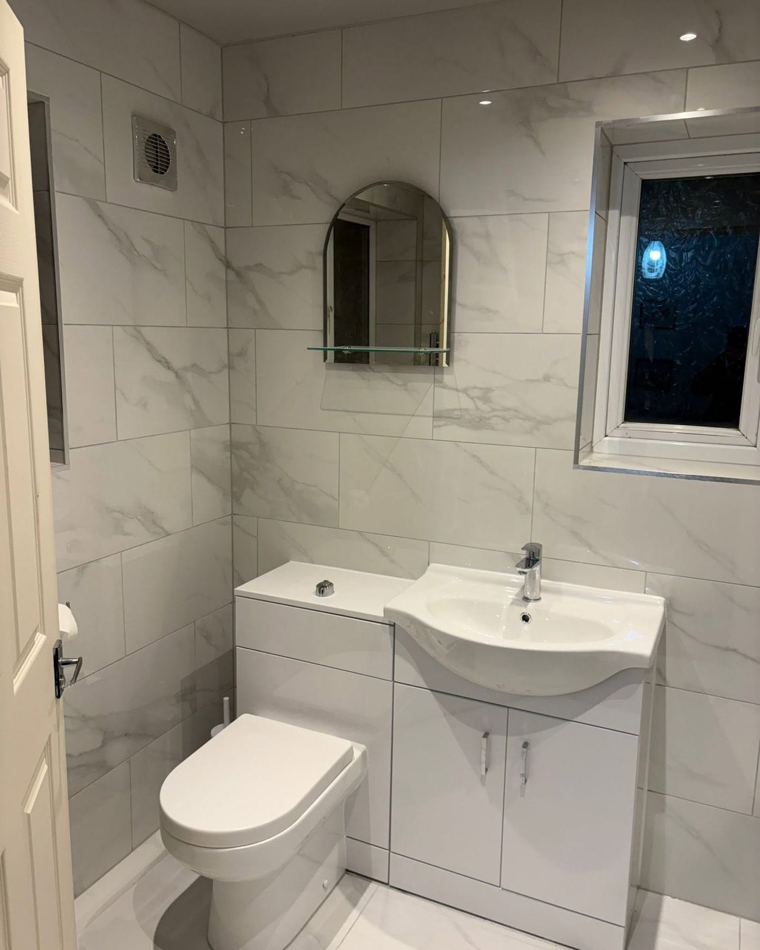 Completed bathroom fit-out with vanity unit, toilet, mirror and tiled walls