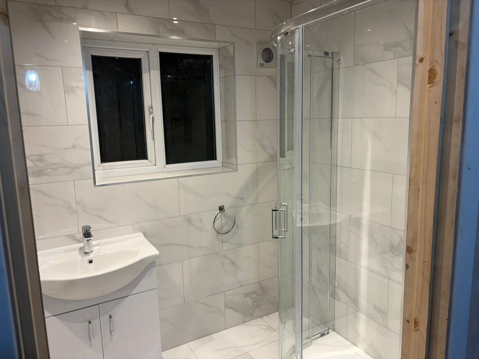 Fitted bathroom with glass shower enclosure, tiled walls and chrome fittings